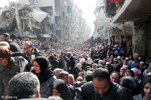 Miles de personas refugiadas hacen cola para recibir la ayuda alimentaria de Naciones Unidas (UNRWA) en el campamento de Yarmouk, al sur de...