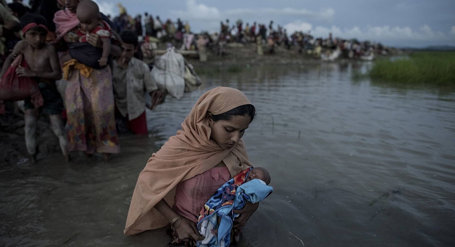 Personas refugiadas rohingyas cruzan a pie un río 
