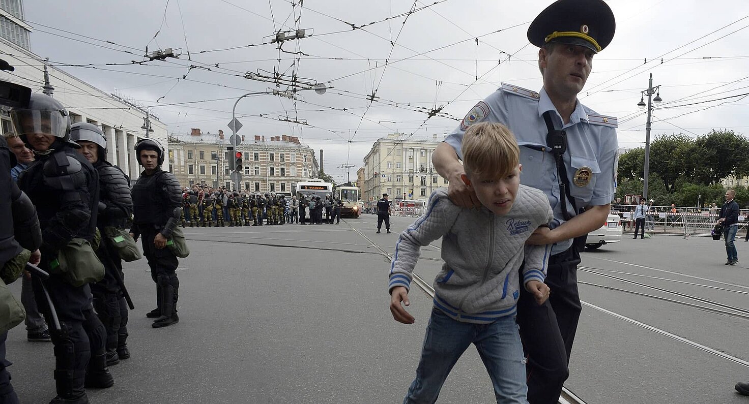 Un agente de policía ruso escolta a un niño durante una concentración de protesta