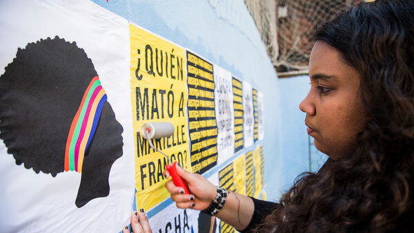 Mujer joven pegando un cartel que pregunta Quién asesinó a Marielle Franco