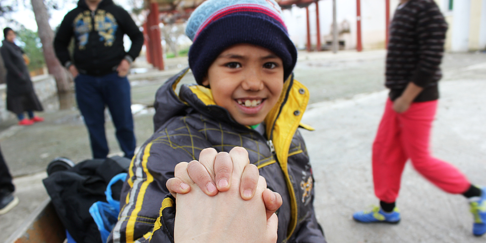 Un niño refugiado sonriente agarra la mano del fotógrafo