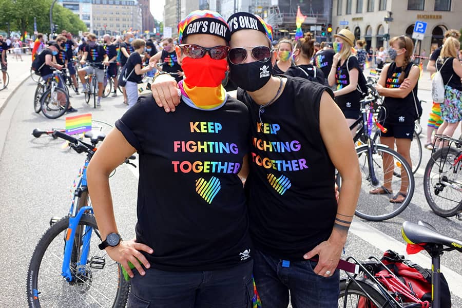 Dos personas en la Marcha del Orgullo con una camiseta en la que se puede leer "Keep fighting together"