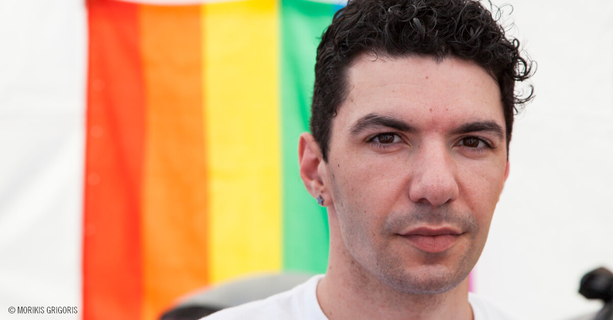 Retrato de Zak Kostopoulos delante de una bandera arcoiris