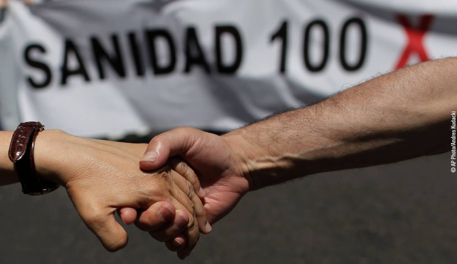 Dos manos unidas delante e una pancarta por la sanidad