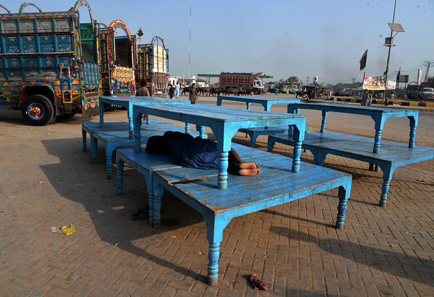 Un camionero se echa una siesta bajo las mesas apiladas en medio del calor abrasador