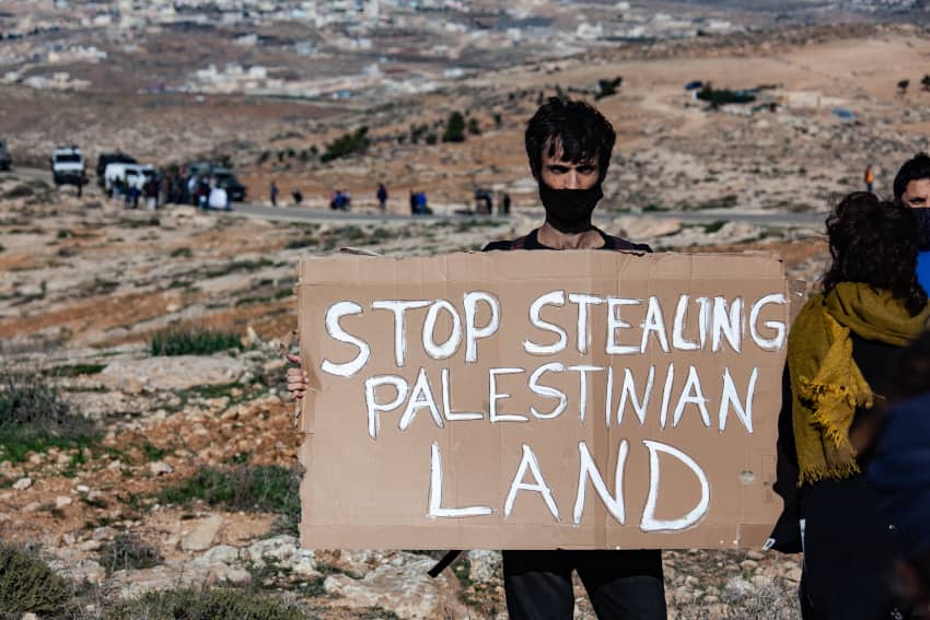Persona sostiene un cartel con el mensaje “Stop stealing Palestinian land” durante una protesta en Cisjordania contra las demoliciones y el robo de tierras palestinas por parte de Israel.