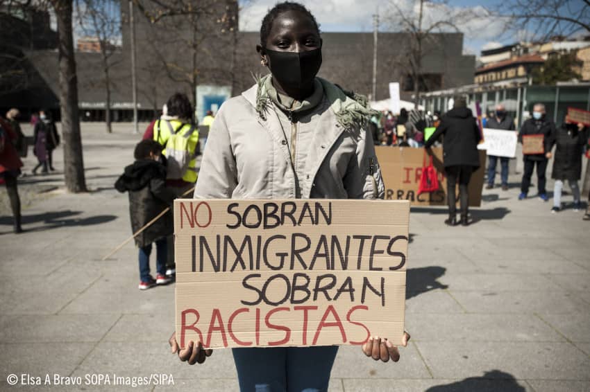Una joven negra sostiene un cartel que dice "No sobran inmigrantes, sobran racistas"