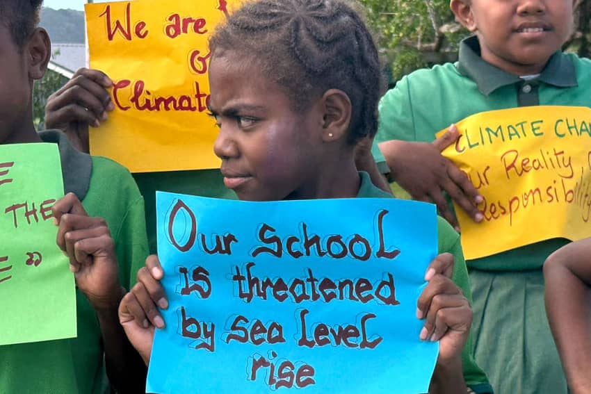 Niña de una isla del Pacífico sostiene un cartel que advierte que su escuela está amenazada por el aumento del nivel del mar.