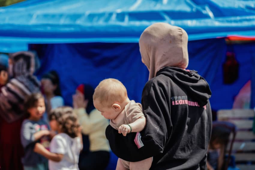 Mujer sostiene a un bebé frente a un campamento de desplazados donde viven familias refugiadas en Beirut.