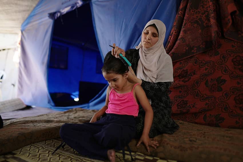 Madre peina a su hija dentro de una tienda de campaña en un campamento de desplazados en Gaza tras perder su hogar.