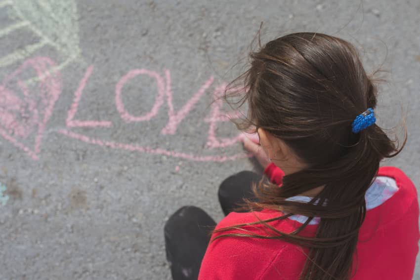 Niña escribiendo la palabra “LOVE” con tiza en el suelo, imagen asociada a la protección y el bienestar infantil.