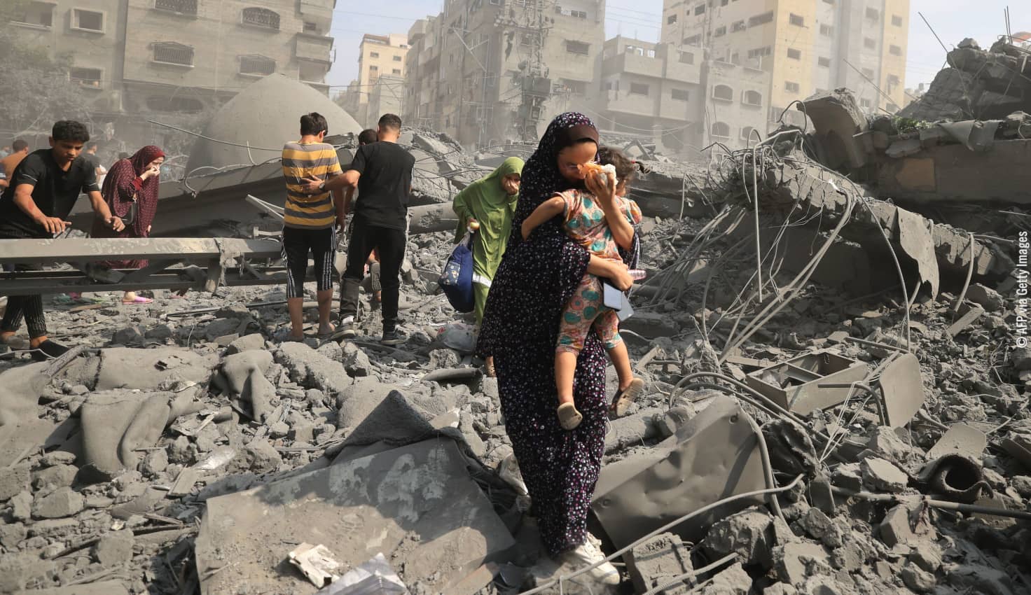 En primer plano una mujer palestina con un niño en brazos huye de una zona atacada