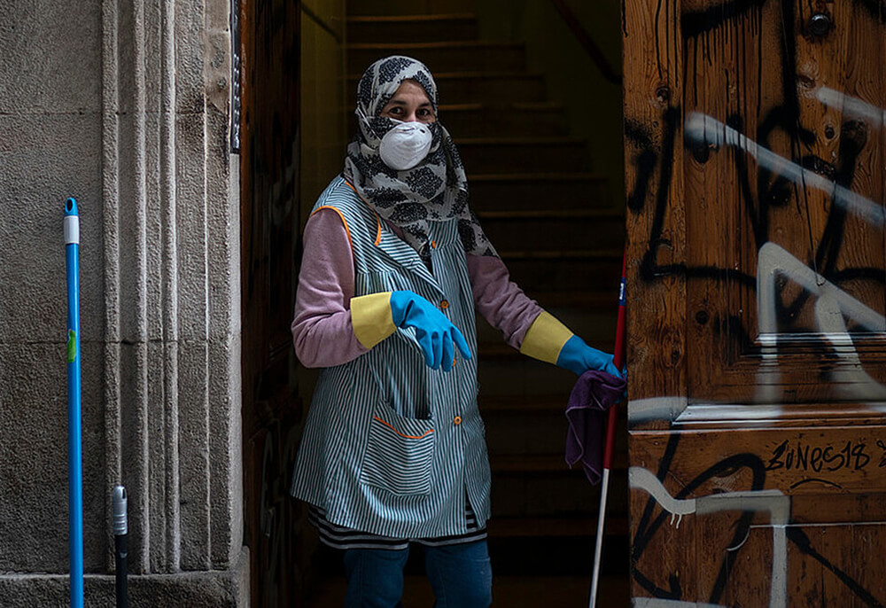Una mujer con mascarilla y guantes se toma un descanso mientras limpia la entrada de un edificio en Barcelona, ​​24 de marzo de 2020.
