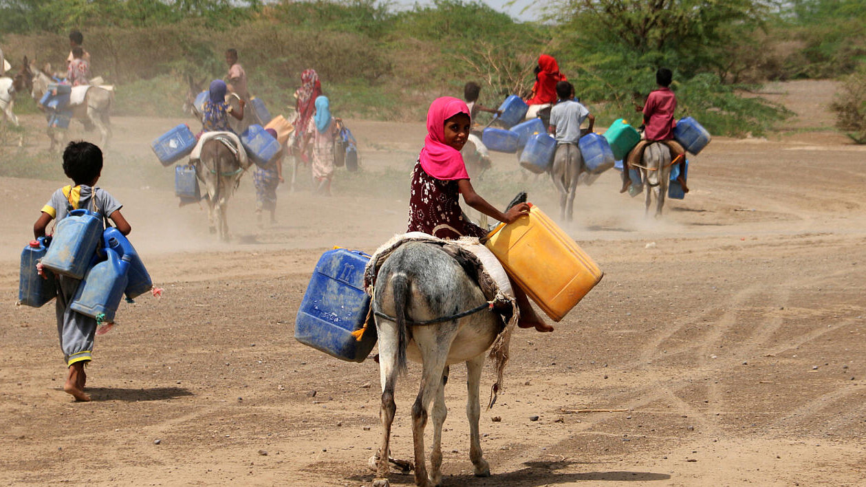 Niñosy niñas en zona desértica con garrafas para transportar agua