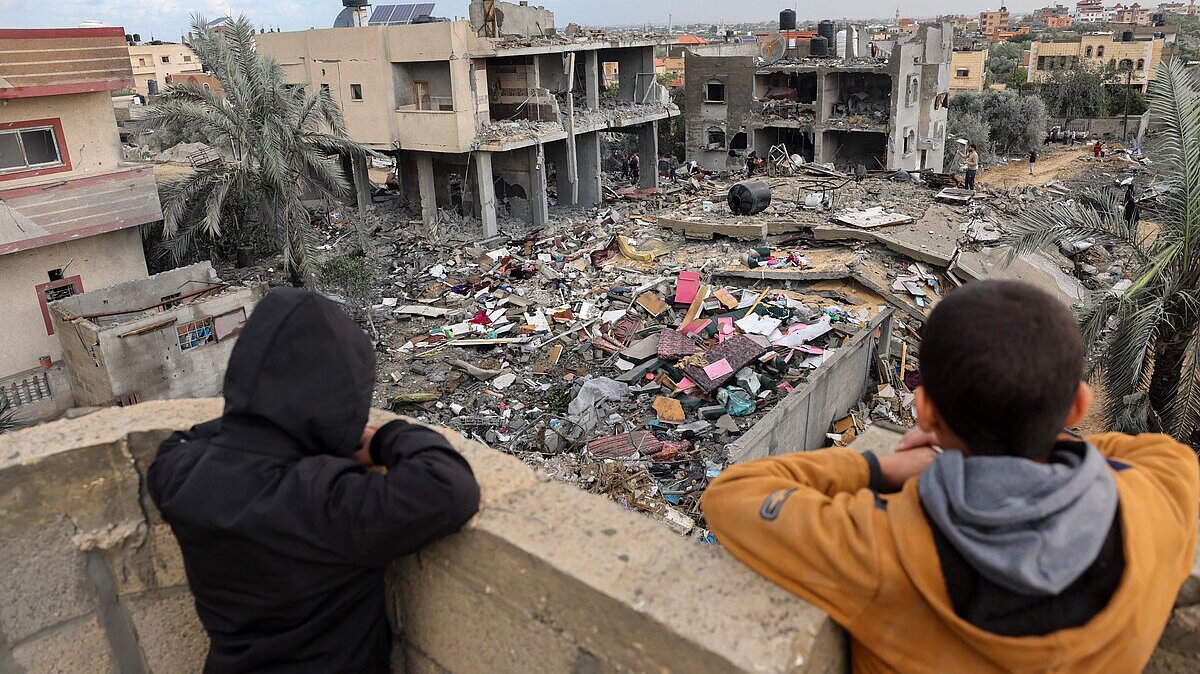 Niños palestinos mirando como la gente recupera objetos entre los escombros de edificios derruidos