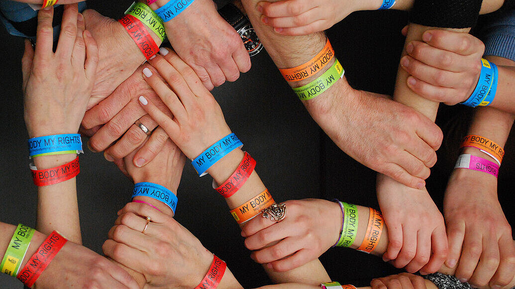 Activistas de Amnistía Internacional Suiza, con manos entrecruzadas en las que se ven pulseras de la campaña "Mi cuerpo, mis derechos"