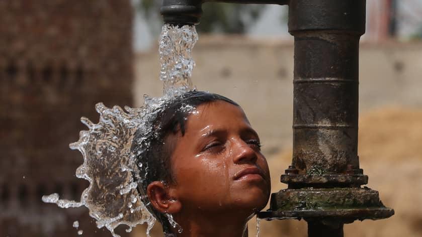 Un niño se refresca con una bomba manual de agua