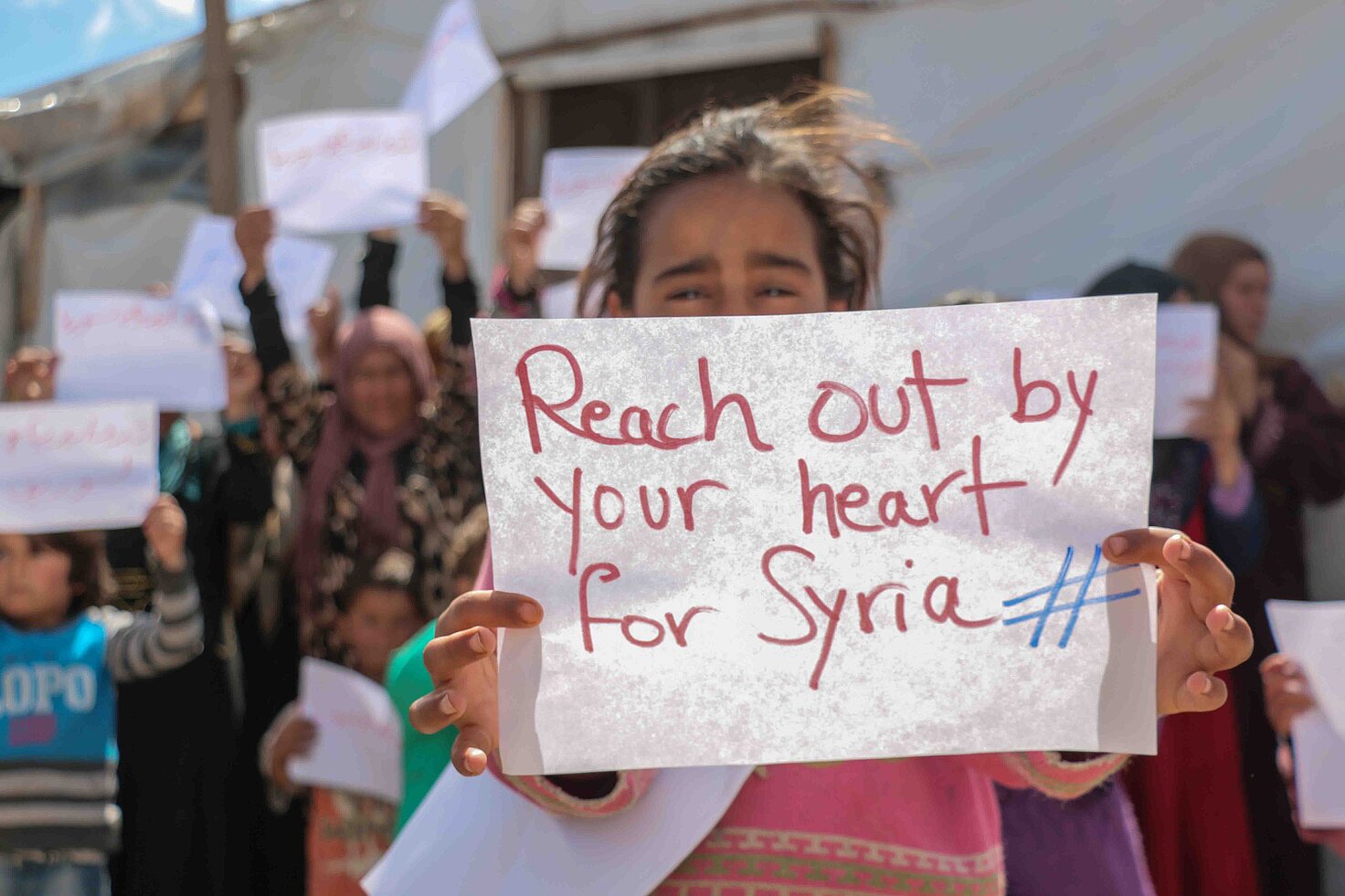 Una niña siria sostiene un cartel de apoyo a la población civil siria.