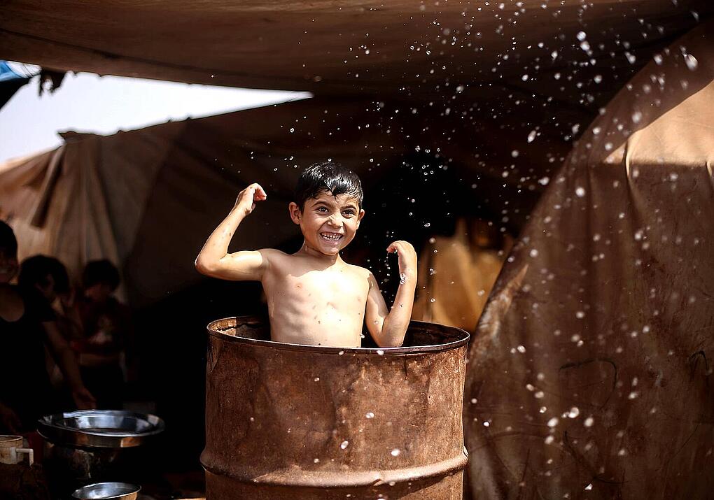 Imagen de un niño refugiado jugando con agua. Enfrentemos las frases racistas con palabras de inclusión, justicia y solidaridad