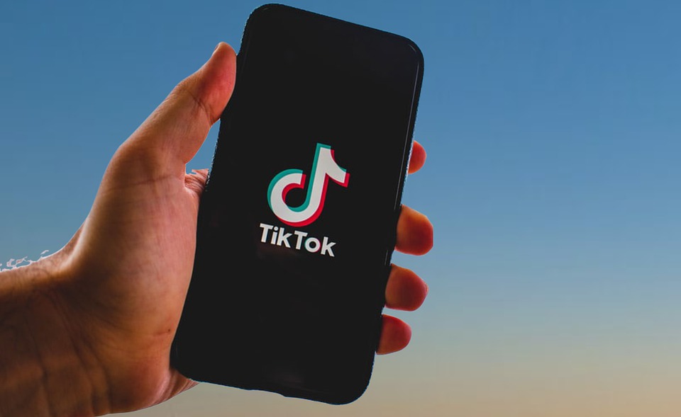 Man a suxeitar un teléfono móbil en que se ve o símbolo de TikTok © Nikuga/Pixabay