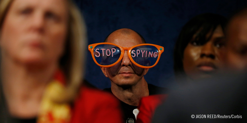 Un manifestante portando unas grandes gafas que dicen "Dejen de espiar"