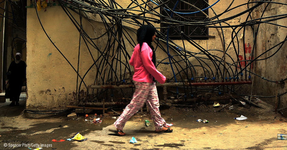 Una mujer camina en un barrio pobre junto a uan red de mangueras