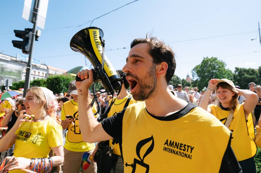 Activistas vestidos con camisetas amarillas de Amnistía Internacional participan en la Marcha del Orgullo de Budapest, levantando sus brazos en...
