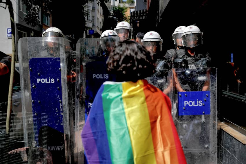 Manifestante portando bandera arcoíris se enfrenta a línea de policías antidisturbios durante una protesta por derechos LGBTIQ+ reprimida en...