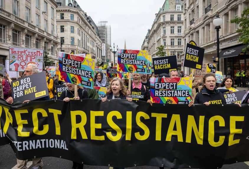 Manifestación de Amnistía Internacional en Londres con una pancarta de “Expect resistance” y carteles de “Resist racism” contra el racismo y en...