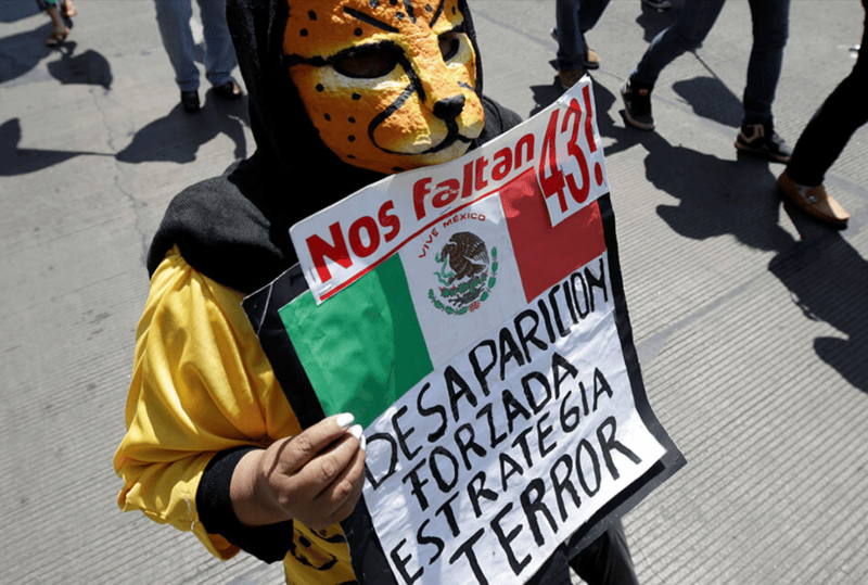 Un niño disfrazado sostiene una pancarta que pone "Desaparición forzada, estrategia de terror" 