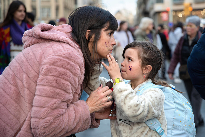 Niña pintando el símbolo feminista en el rostro de una mujer durante una manifestación por los derechos de las mujeres en Barcelona