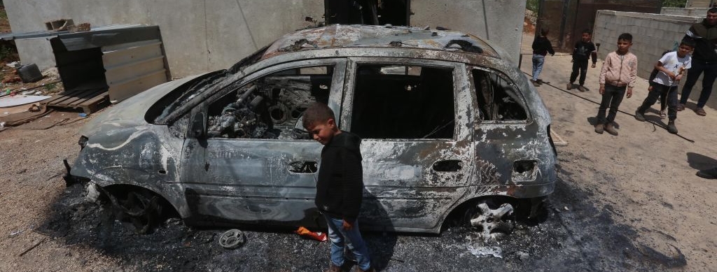 un niño palestino frente a un coche calcinado