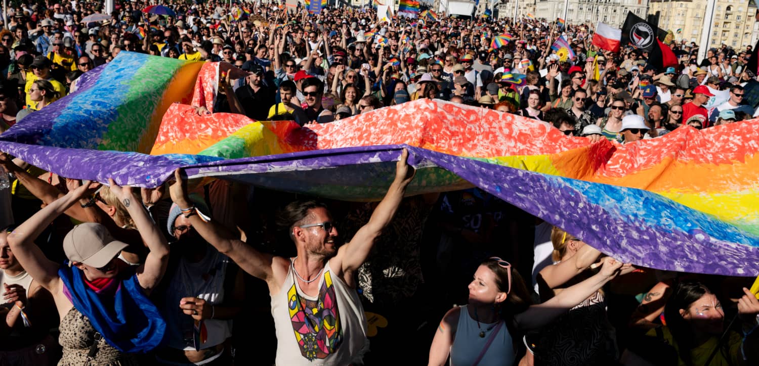 Miles de personas participan en la marcha del Orgullo LGBTIQ+ en Budapest bajo una gran bandera arcoíris.