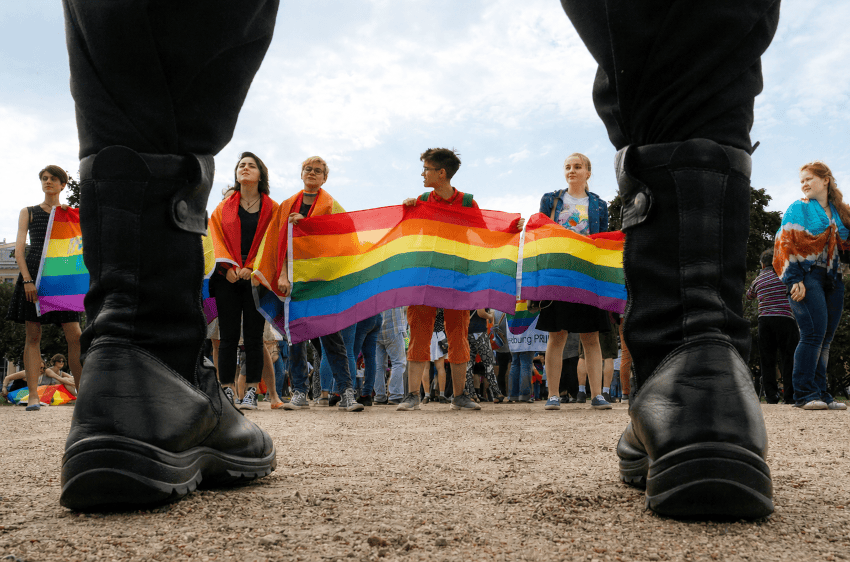 Personas con una bandera arcoíris participan en una marcha del Orgullo frente a un cordón policial.