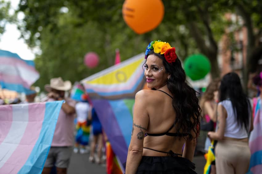 Una mujer participa en una marcha del Orgullo rodeada de banderas y símbolos de la diversidad.