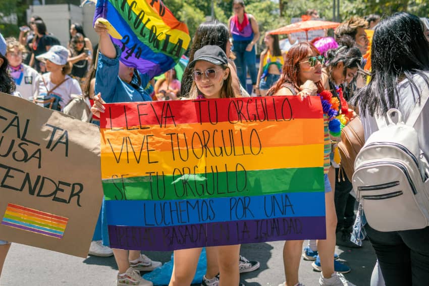 Persona sostiene una pancarta con los colores del arcoíris y mensajes sobre el orgullo y la igualdad durante una manifestación del Orgullo.