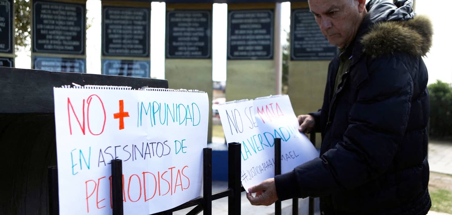 Un hombre coloca varios carteles que denuncian la impunidad en los asesinatos de periodistas