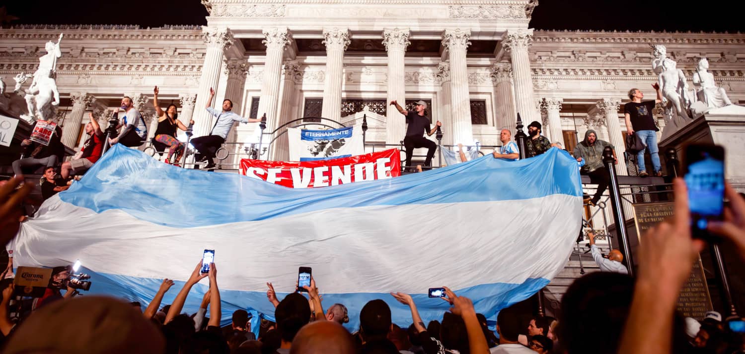 Manifestantes sosteniendo una gran bandera argentina frente al Congreso durante una protesta contra las políticas de Javier Milei en Buenos Aires.
