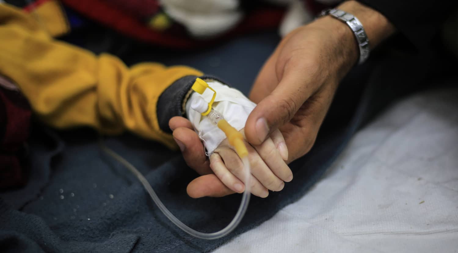 Mano de un niño con vía intravenosa sostenida por un adulto en Gaza