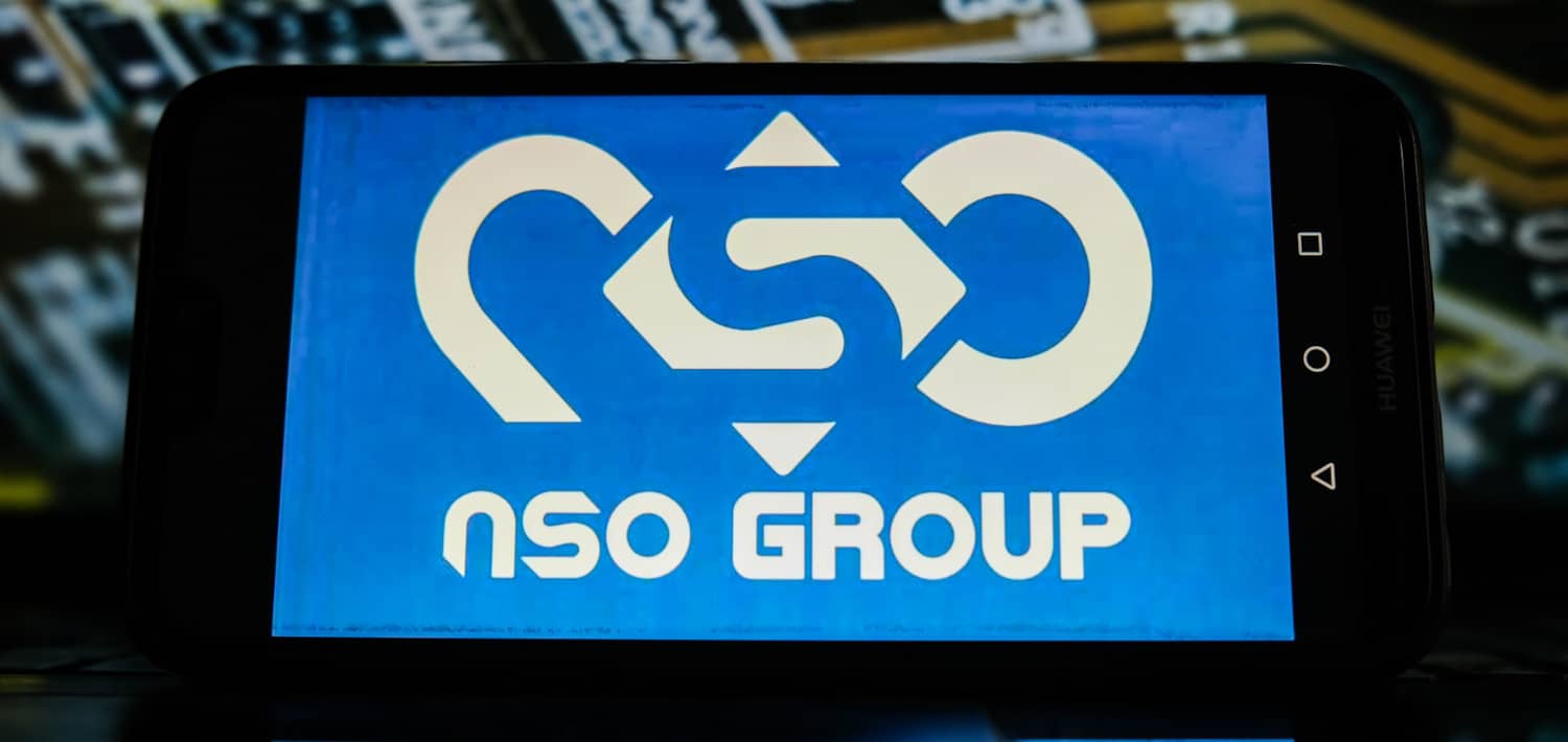 Logotipo de NSO Group sobre fondo azul en la pantalla de un teléfono colocado en horizontal.