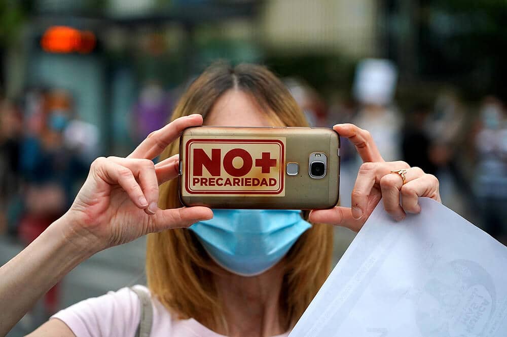 Mujer en una manifestación en defensa de la sanidad porta un teléfono móvil con una funda en la que se puede leer el mensaje "No + Precariedad"