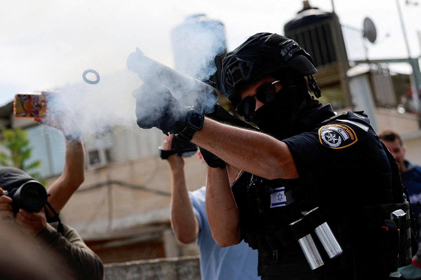 Un agente de la policía fronteriza israelí dispara un bote de gas antidisturbios, mientras palestinos musulmanes intentan celebrar la oración del...