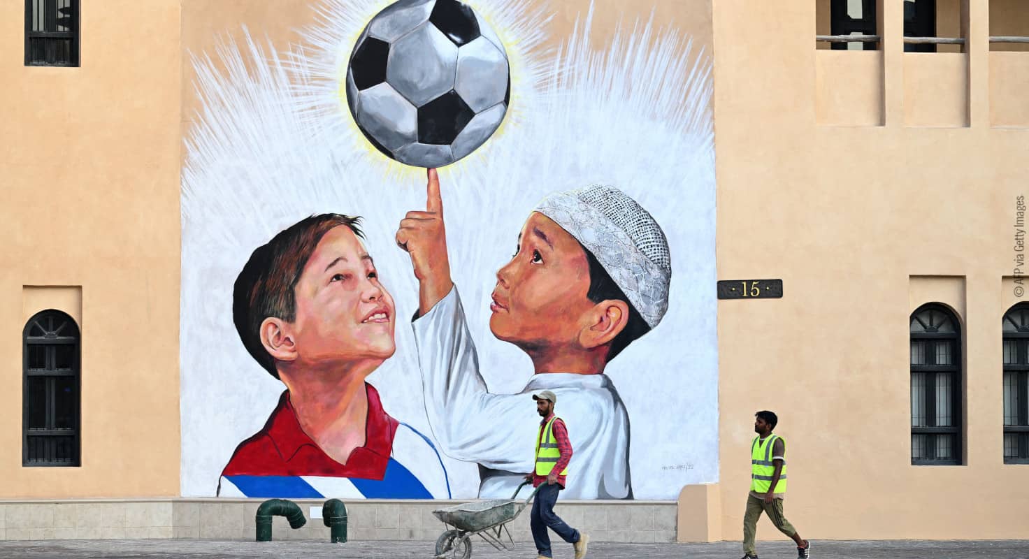 Un trabajador empuja una carretilla frente a un mural en que aparecen dos niños con un balón
