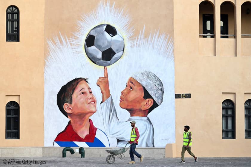 Un trabajador empuja una carretilla frente a un mural en que aparecen dos niños con un balón