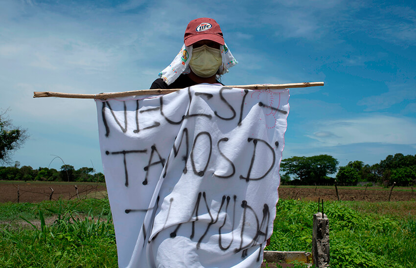 Una trabajadora de una fábrica que fue despedida temporalmente muestra en una carretera una bandera blanca improvisada que reza "Necesitamos su ayuda" mientras pide comida durante la cuarentena obligatoria decretada por el gobierno contra la propagación de la COVID-19 en San Luis Talpa, El Salvador. el 29 de mayo de 2020 