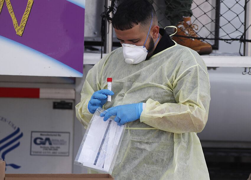Un técnico médico en un centro de pruebas COVID-19 de Stride Community Health Center carga un vial que contiene un hisopo de un kit de prueba en un sobre