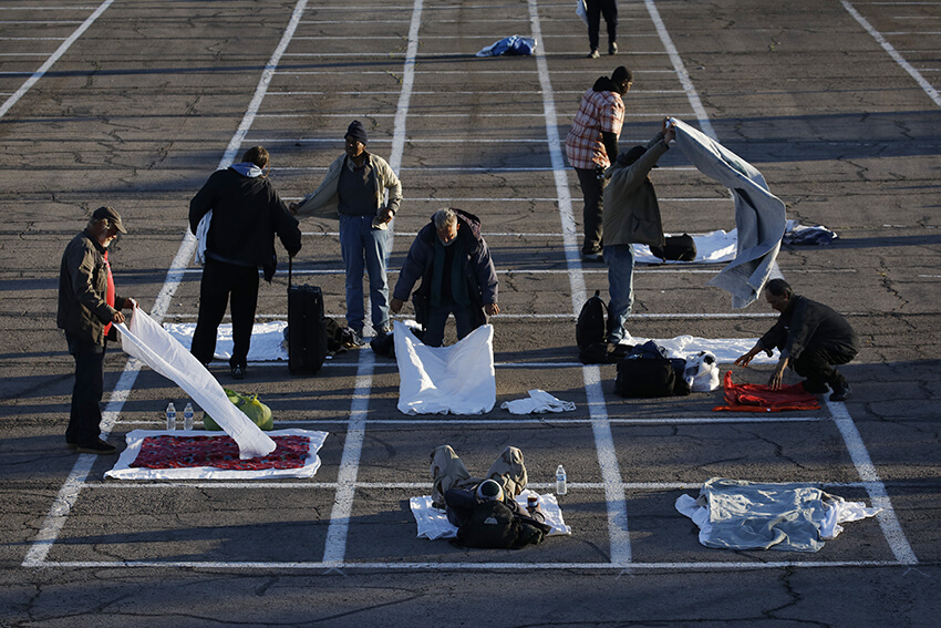 La gente prepara lugares para dormir en un área marcada por cajas pintadas en el suelo de un estacionamiento en un campamento improvisado para personas sin hogar el lunes 30 de marzo de 2020 en Las Vegas