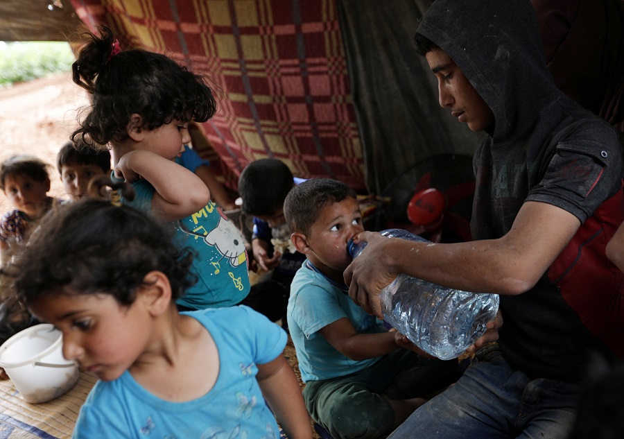 Un niño sirio desplazado bebe agua con la ayuda de otro miembro de la familia en un olivar en la ciudad de Atmeh, provincia de Idlib, Siria