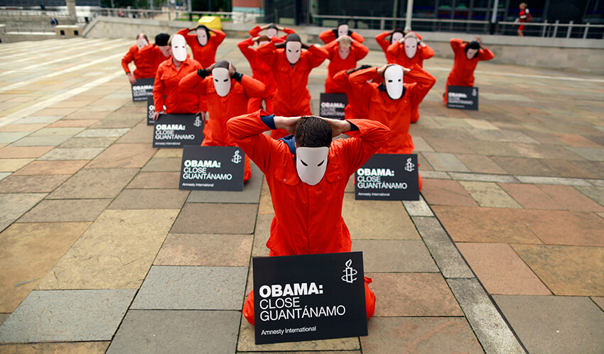 Activistas de Amnistía Internacional enmascarados y vestidos como detenidos de Guantánamo participan en una performance para pedir el cierre de la base naval.