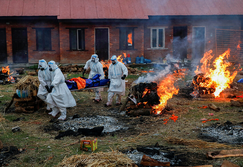 Personal con equipo de protección pasan junto al fuego mientras se incineran los cuerpos de las personas fallecidas a causa de la COVID-19 en Katmandú, Nepal,